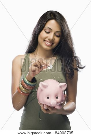 Young woman putting a coin into a piggy bank