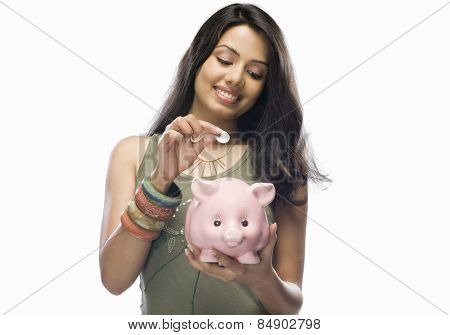 Young woman putting a coin into a piggy bank