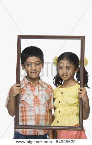 Portrait of a boy and a girl holding an empty picture frame