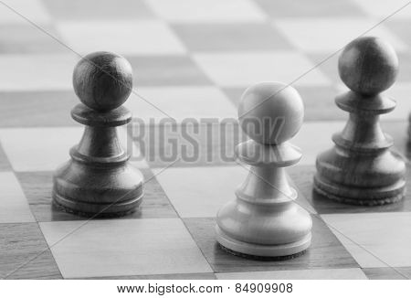 White chess pawn near two black chess pawns on a chess board