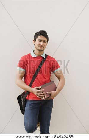 Man leaning against a wall and holding books