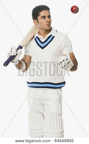Cricket batsman holding a bat and looking at a ball