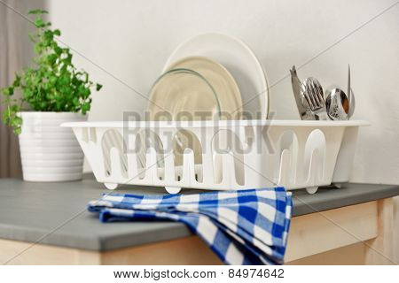 Dish drainer with plates and silverware on a table. Focus on the dish drainer