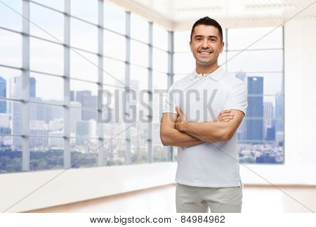 happiness, real estate and people concept - smiling man in white t-shirt over empty apartment or office room with big window and city view background