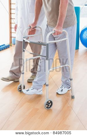 Senior man on zimmer frame with therapist in fitness studio
