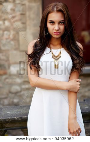 Fashionable gorgeous female model with beautiful curly hair in white dress looking to the camera