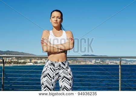 Healthy young woman in sports clothing with her arms crossed standing on sky background outdoors