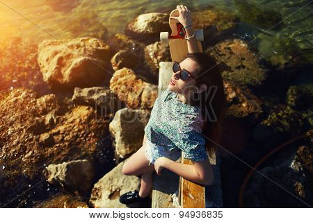 Young woman posing with her skateboard in front of the sea while enjoying summer sunshine