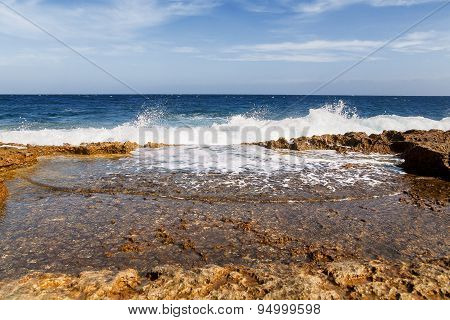 The Waves Beat Against The Rocky Shore. Water Flooded Depressions In The Rocks. Malta, Saint Julians