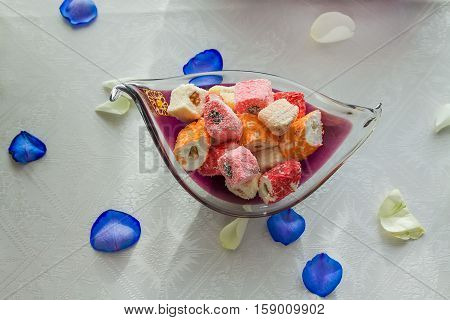 Colorful turkish delight in vase with blue and white rose petals on white tableclothe