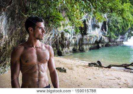 Half body shot of a handsome young man standing on a beach in Phuket Island, Thailand, shirtless wearing boxer shorts, showing muscular fit body