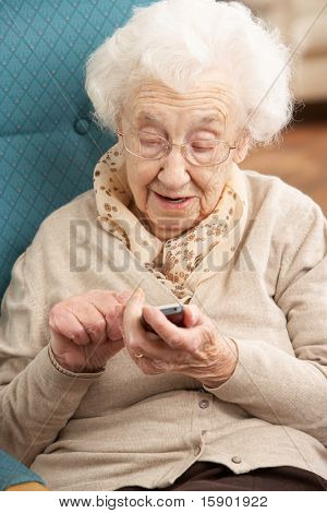 Senior kvinde-nummer på mobiltelefon sidder i stolen i hjemmet
