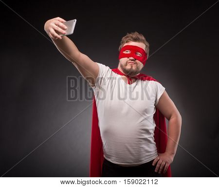 Egoist. Self. Hero. Super Hero. Handsome super hero man making photos on his mobile or smart phone isolated on black in studio.