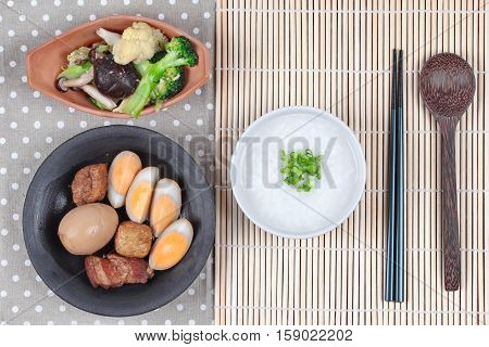 Rice gruel and stewed boiled egg with tofu and streaky pork and fried mixed vegetable served .
