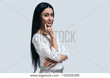 Thinking about new business aproaches. Confident young woman in white shirt smiling and looking at camera while standing against grey background