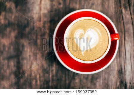 Red cup of cappucino with beautiful latte art on old wooden background. Top View.