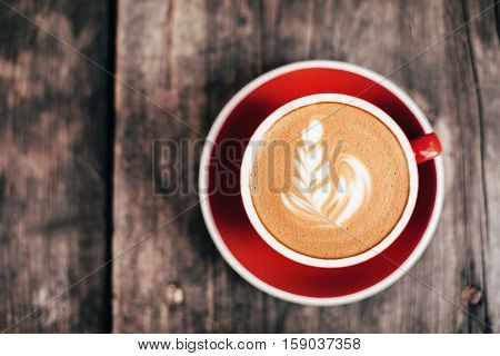 Red cup of cappucino with beautiful latte art on old wooden background. Top View.