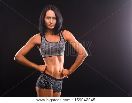 Sports and fitness concepts. Brunette fitness lady in sports costume posing with her hands on hips and demonstrating her perfect body in studio.