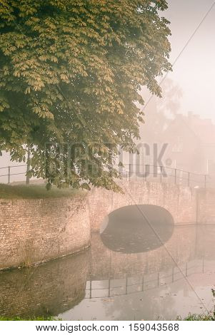 Old fortress bridge over the canal of the park is reflected in the misty quiet water