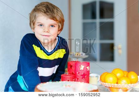 Beautiful little kid boy standing by festive table at Christmas time and holding candle. Excited child celebrating traditional . Xmas party. Catholic and christian celebration in Europe and USA