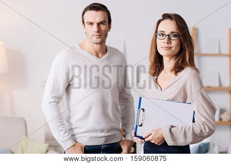 Ready to help you. Pleasant delighted professioanl psychologist standing with handsoem senior man while going to solve problems