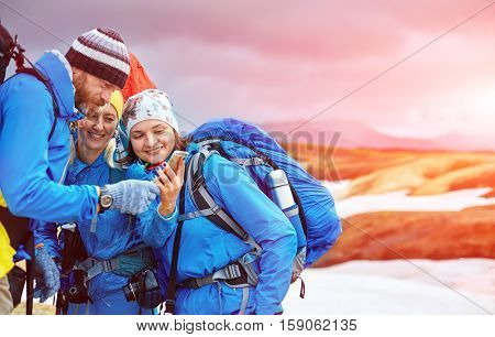 couple friends hikers un the Islandic mountains. two woman and one man photographer taking picture on the rhyolite mountains background in Iceland. people looking at the smartphone and laughs