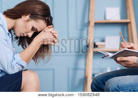Hopeful and desperate. Depressed young woman sitting o the couch and leaning forward while consulting with professioanl psychotherapist