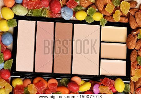 Cosmetic powder and mix of dragee with raisins or peanuts inside marmalade or jelly candies almonds on colorful background