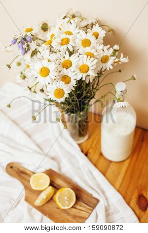 Simply stylish wooden kitchen with bottle of milk and glass on table, summer flowers camomile, healthy foog moring concept noone