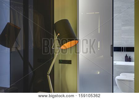 Glowing design lamp on the background of the entrance to the modern bathroom with a glassy door. Bathroom tiled with gray and white tiles. There is a white bath, white toilet and a bide. Horizontal.