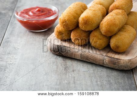 Traditional fried Spanish croquetas (croquettes) with ketchup on wooden background