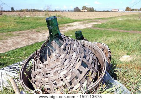 Old demijohn glass wrapped in wicker abandoned
