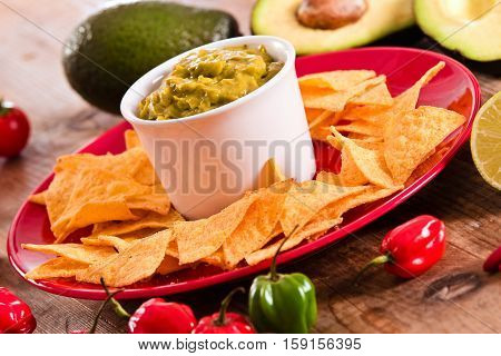 Guacamole and nacho chips on red dish.