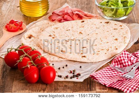 Piadina with ham and lettuce on wooden table.