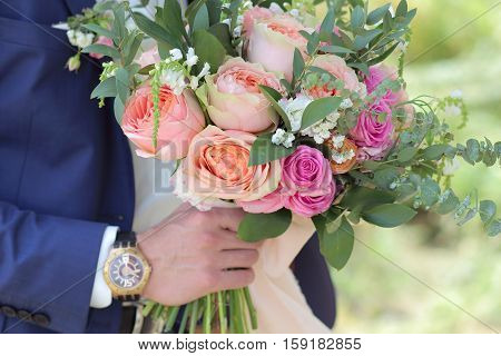 Beautiful bridal bouquet in hands of the groom. Wedding bouquet of peach roses  single-head pink rose aqua eucalyptus ruscus gypsophila
