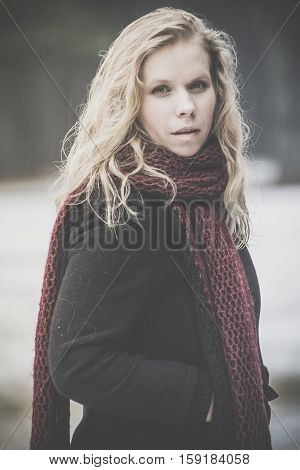 portrait of blond woman with blue eyes on dark background winter girl in black coat, curly hair, blond and beautiful covered with light snow, penetrating eyes, resolute and stern, the photo on street