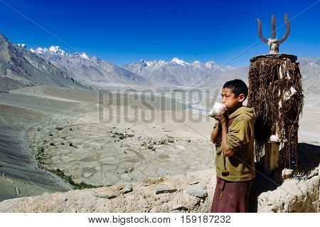PADUM, INDIA - SEPTEMBER 18, 2006: A young monk playing a horn made from a shell. Buddhist monastery of Padum, Ladakh, India.