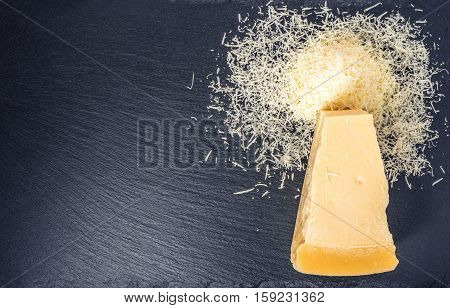 Top Down Of Single Tasty Fresh Yellow Big Segment Piece Of Parm And Finely Grated Cheese On Black Sl