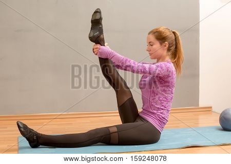 Fit girl sitting with hands and leg up doing lie down leg stretches.