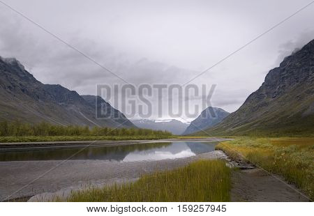 Serene river scenery in mist atmosphere streaming in between rapadalen mountain valley