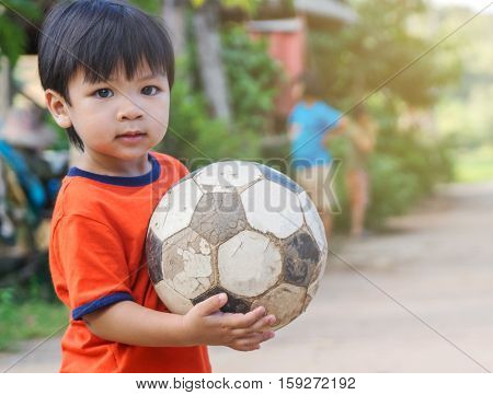 Asian kid in poor village playing with old soccer ball