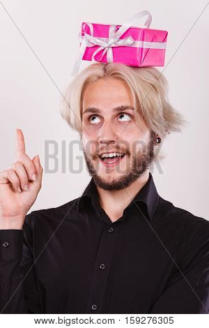 Celebration and giving concept. Cool young man with pink gift box on his head. Guy thinking looking for present idea