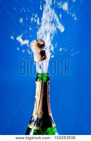 Bottle of champagne with a popping cork (against a bright blue background)