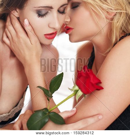 Sensual lesbian lovers whispering in bed with rose foreplay