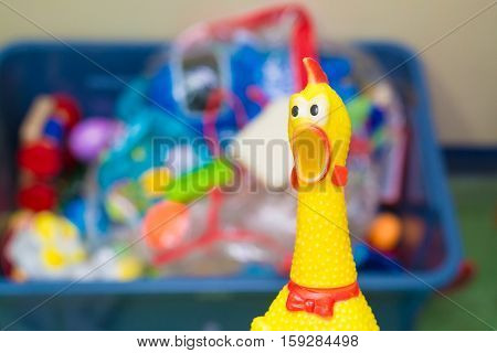 Toy Rubber Shriek Yellow Chicken On Blur Toy Background In Messy Room.