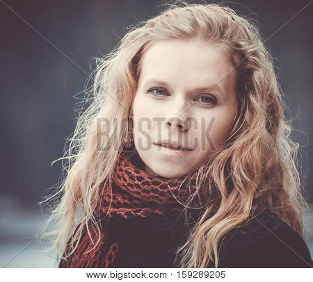 portrait of blond woman with blue eyes on a dark background winter girl in a black coat, curly hair, blond and beautiful, red scarf, light snow, cute look, half-smile, the kindness, photo on street, purple preset processing