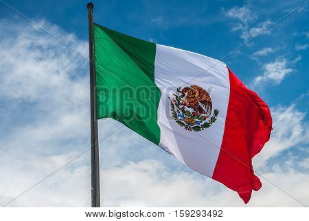 Flag of Mexico over blue cloudy sky