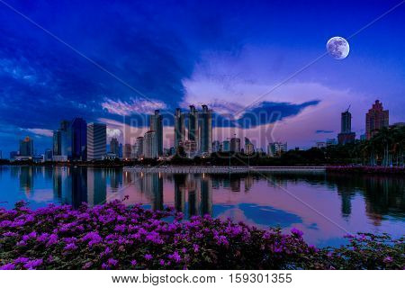 Night Cityscape with Business buildings Light and reflection on the water with moon on the sky from Benjakiti park Bangkok Thailand