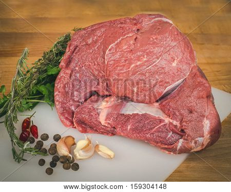 Fresh raw beef on wooden cutting board, spices and herbs. Whole uncooked beef prepare for cooking. Large piece of fresh beef ham.