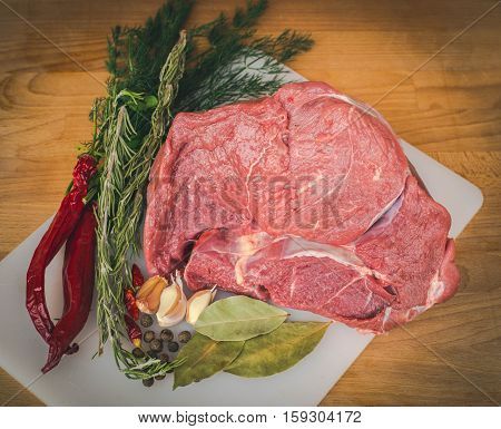 Fresh raw beef on wooden cutting board, spices and herbs. Whole uncooked beef prepare for cooking. Large piece of fresh beef ham.